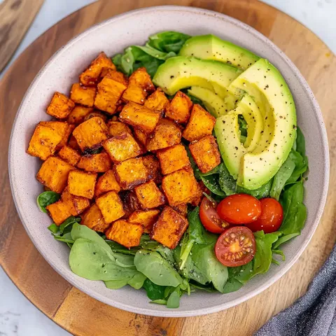 Eine Schüssel mit gewürfelten, gebratenen Süßkartoffeln, Avocado, Cherry-Tomaten und Rucola.