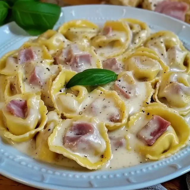 Eine Schüssel mit Tortellini in cremiger Sauce, garniert mit einem Blatt frischem Basilikum.