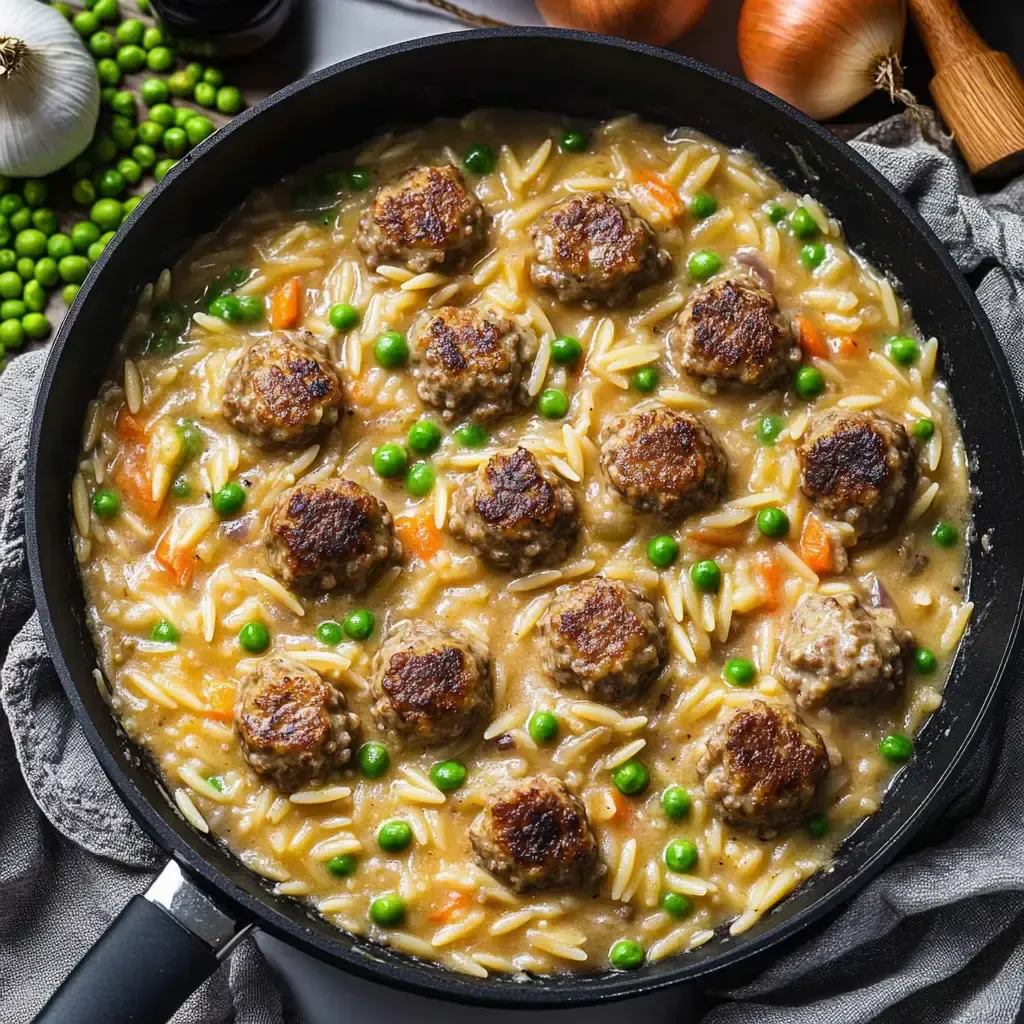 Ein Pfannengericht mit Frikadellen, Reis, grünen Erbsen und Karotten in einer cremigen Sauce.