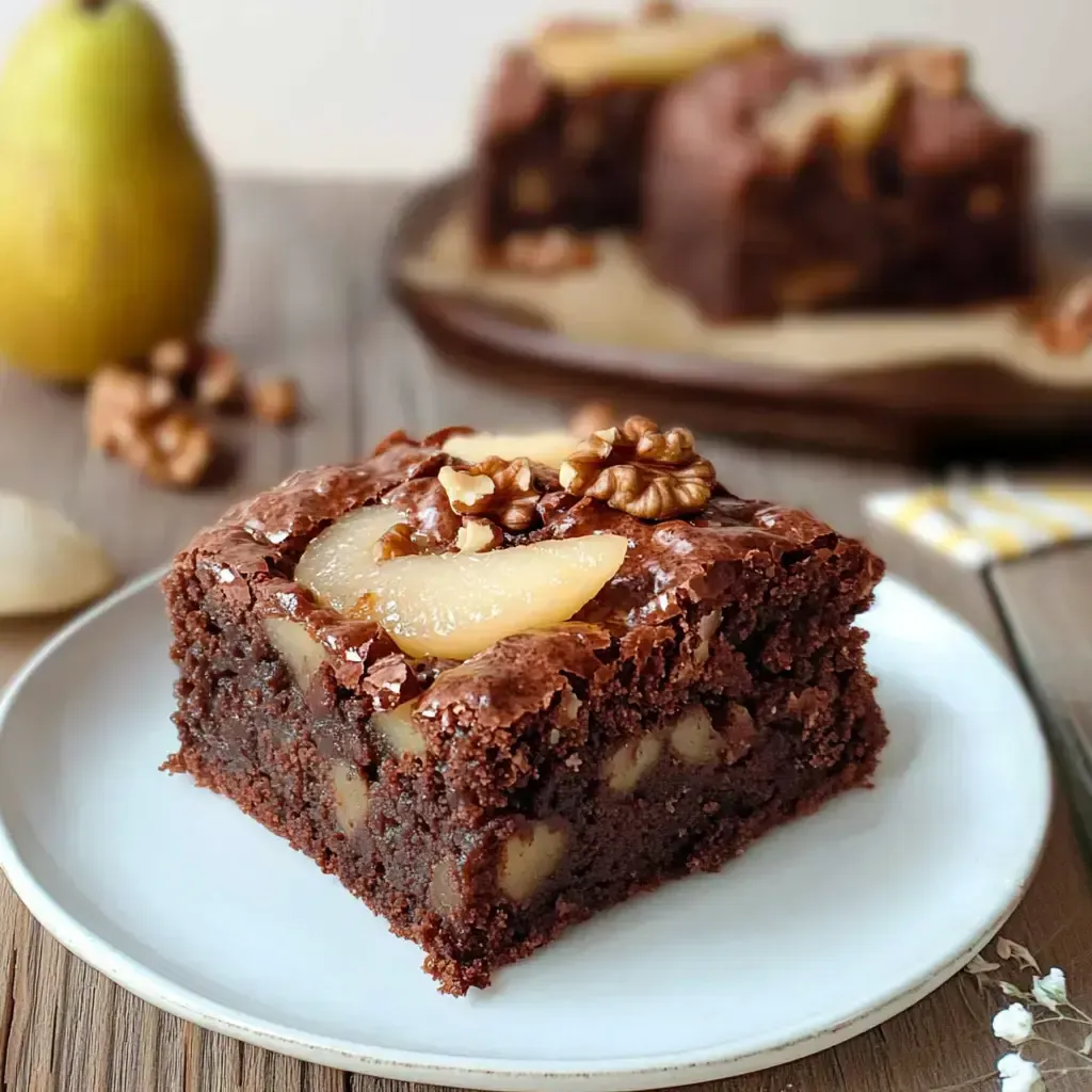 Ein Stück Schokoladenkuchen mit Nüssen und Birnenscheiben auf einem weißen Teller.