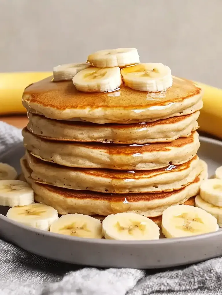 Ein Stapel Pfannkuchen mit Bananenscheiben und Sirup auf einem Teller.