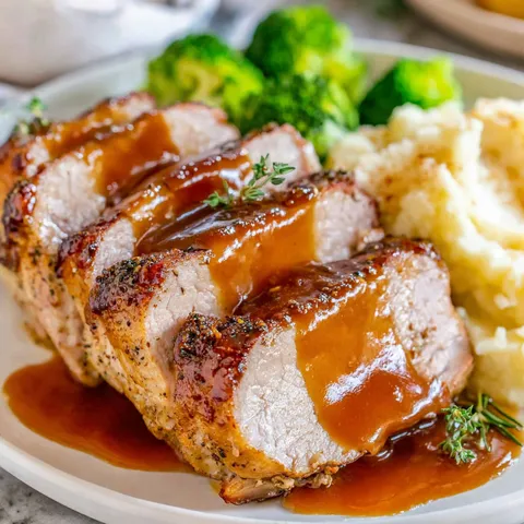 A plate of food with a pork loin roast and gravy.